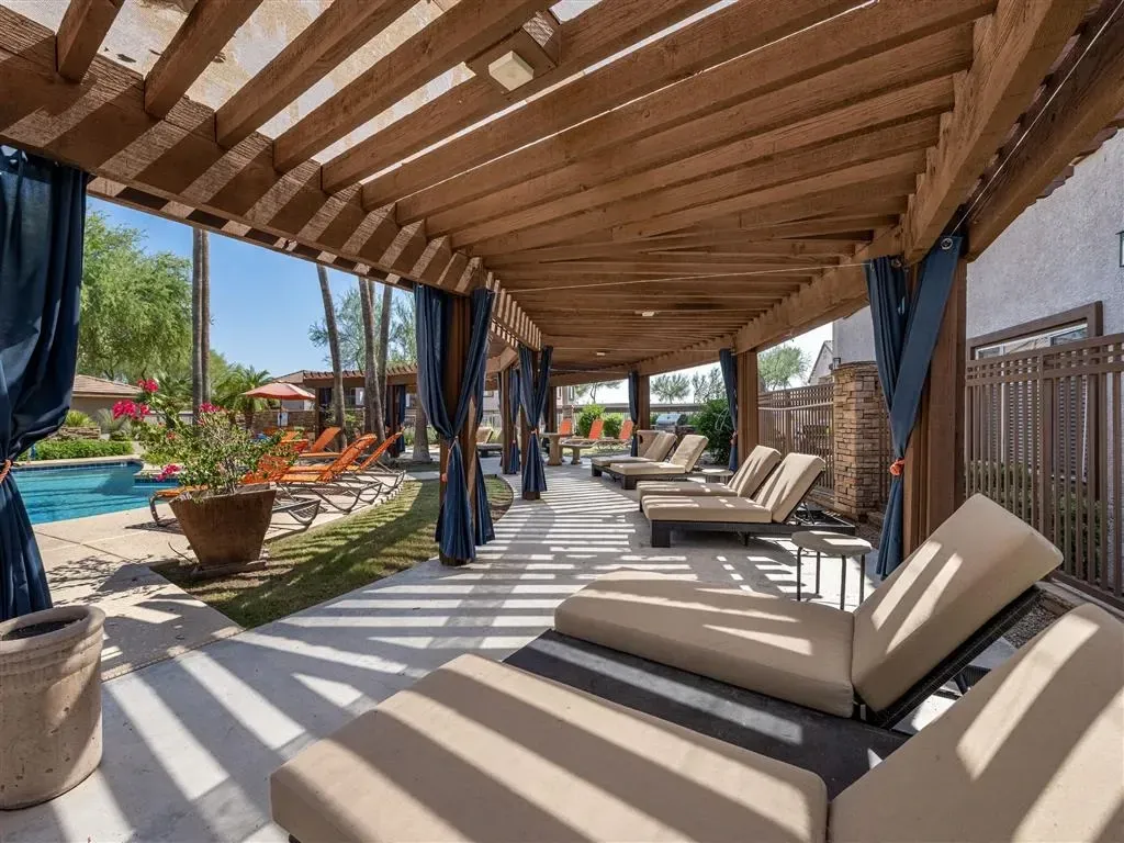 Covered poolside lounge area with chaise lounges and blue drapes.