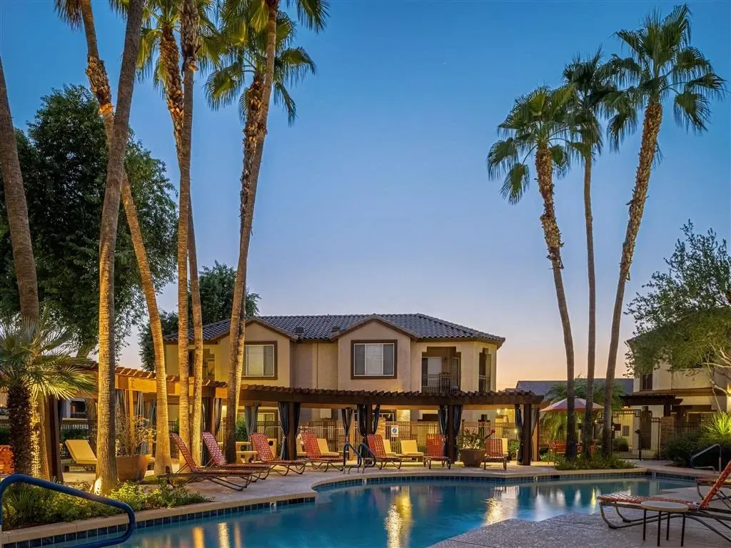 Outdoor swimming pool with lounge chairs and palm trees at dusk.
