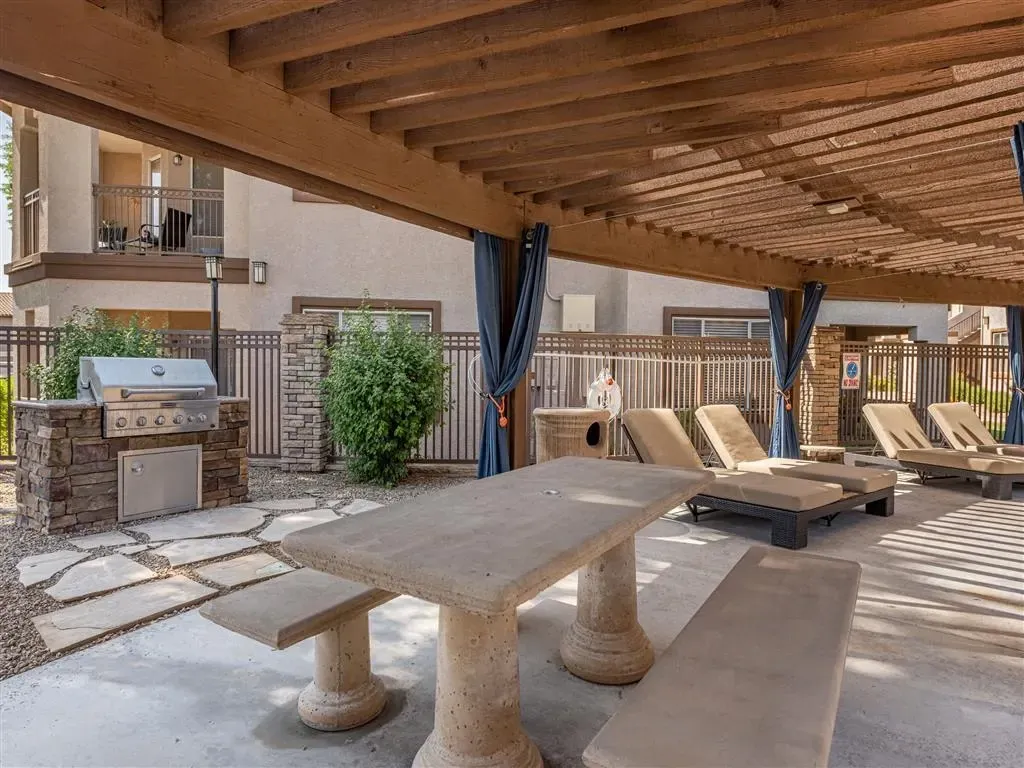 Outdoor grilling station and lounge chairs under a wooden pergola.
