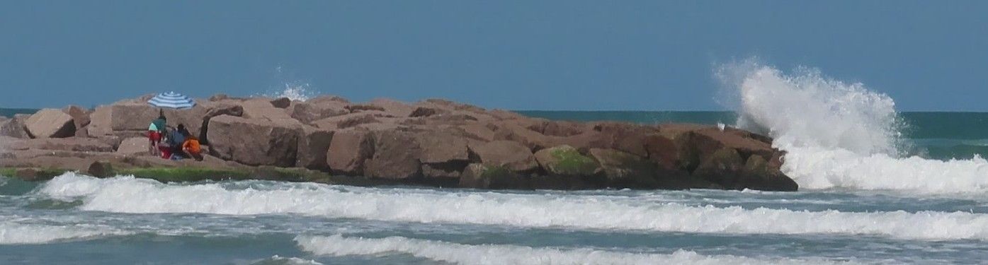 Waves crashing against a rocky jetty on a sunny day.