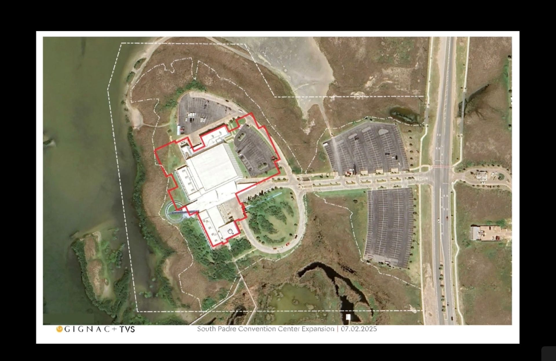 Aerial view of a large commercial building (likely a big box store) with extensive parking and surrounding wetlands.