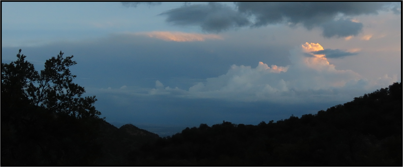 A cloudy sky over a mountain range with trees in the foreground