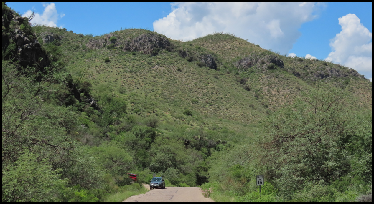 A car is driving down a dirt road in the mountains.