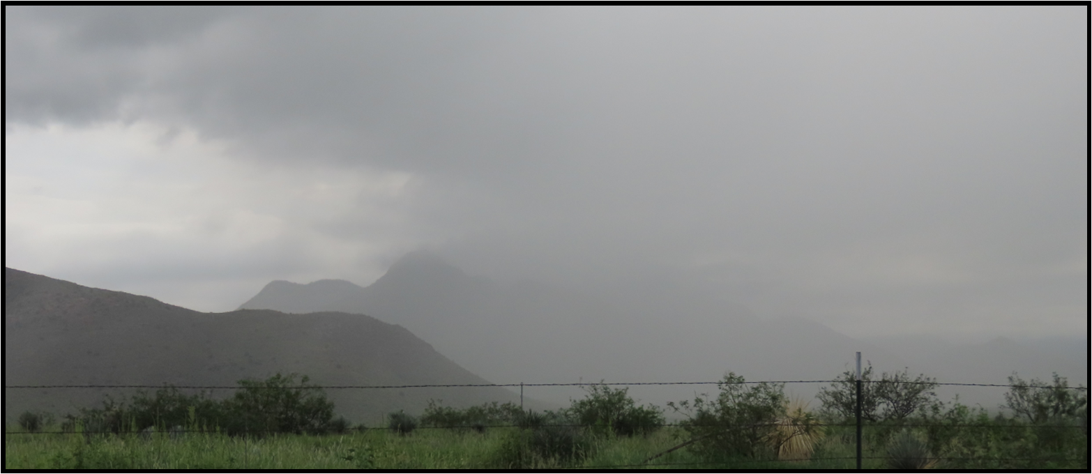 A cloudy sky with mountains in the background and a fence in the foreground.