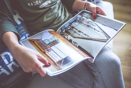 Person holding open a magazine with photos and text while seated on a couch.