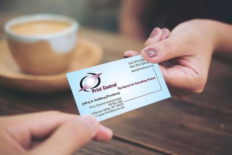 Hands holding a business card over a coffee cup on a wooden table.