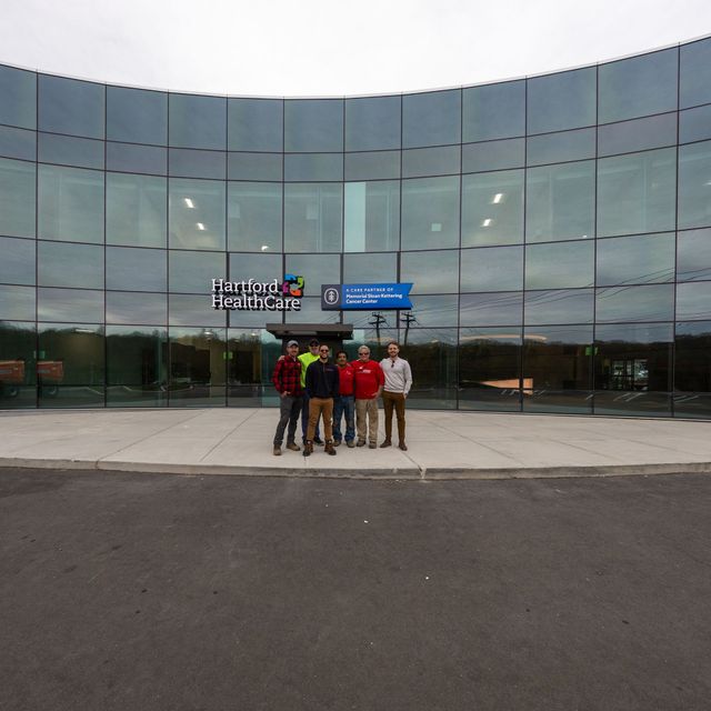 Five people standing in front of a curved glass building with the sign "Easton Area High School".
