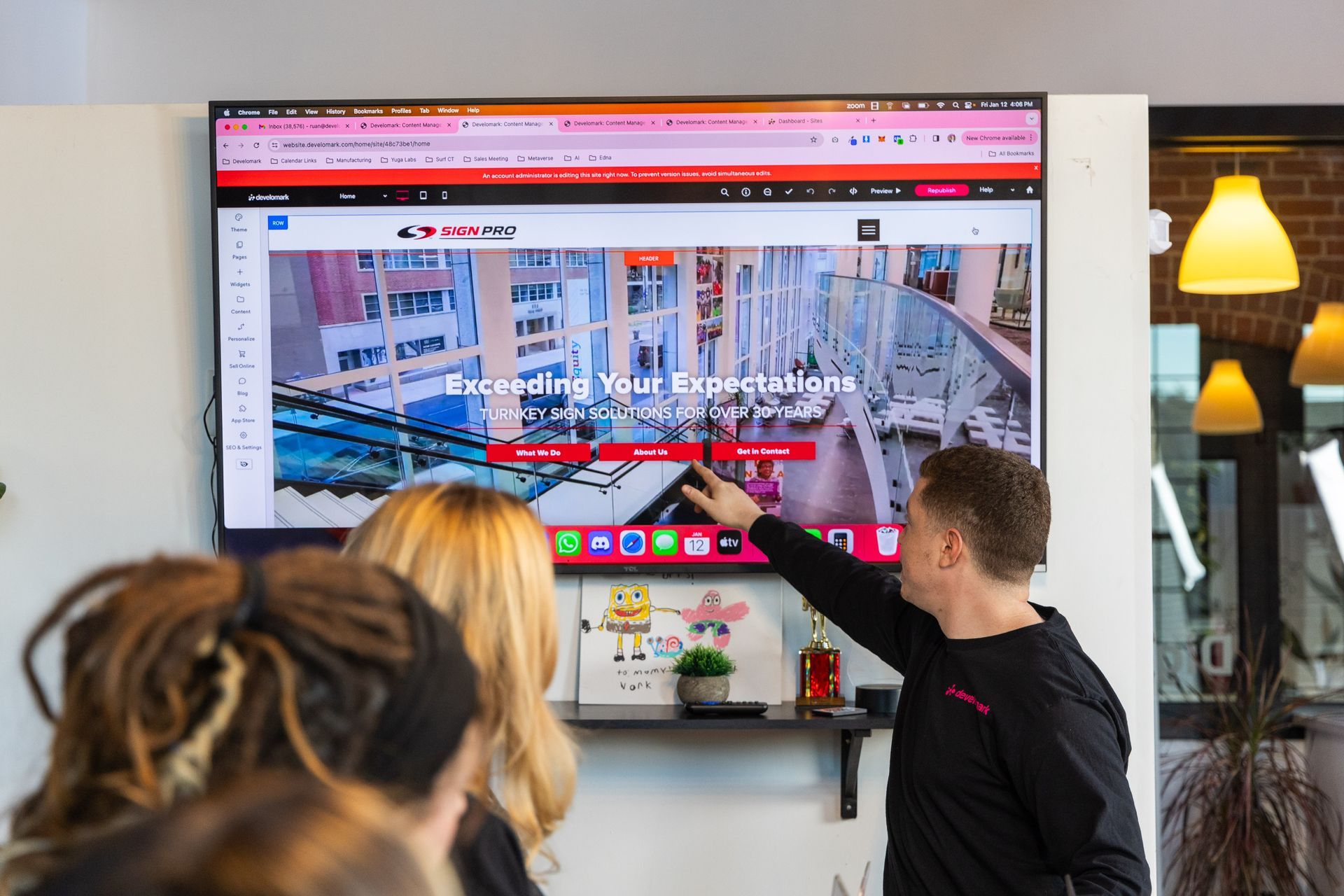 Two people pointing at a large screen displaying a website in a bright office