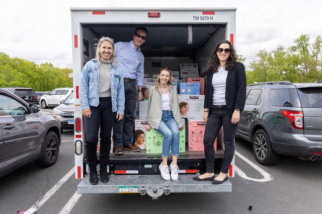 Four people stand at the back of a delivery truck in a parking lot, smiling. Boxes are inside.
