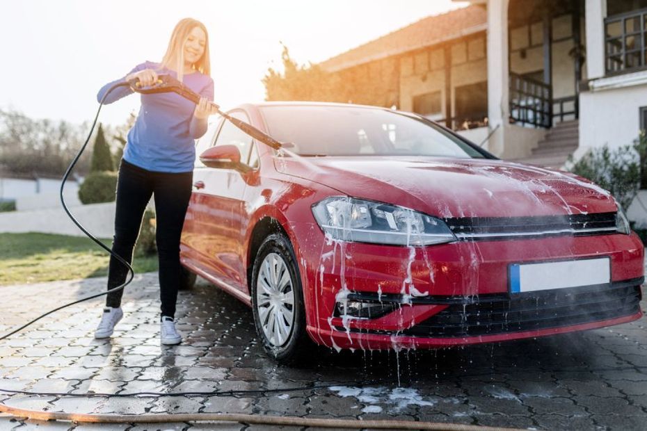 Woman washing a red car with a pressure washer in front of a house.