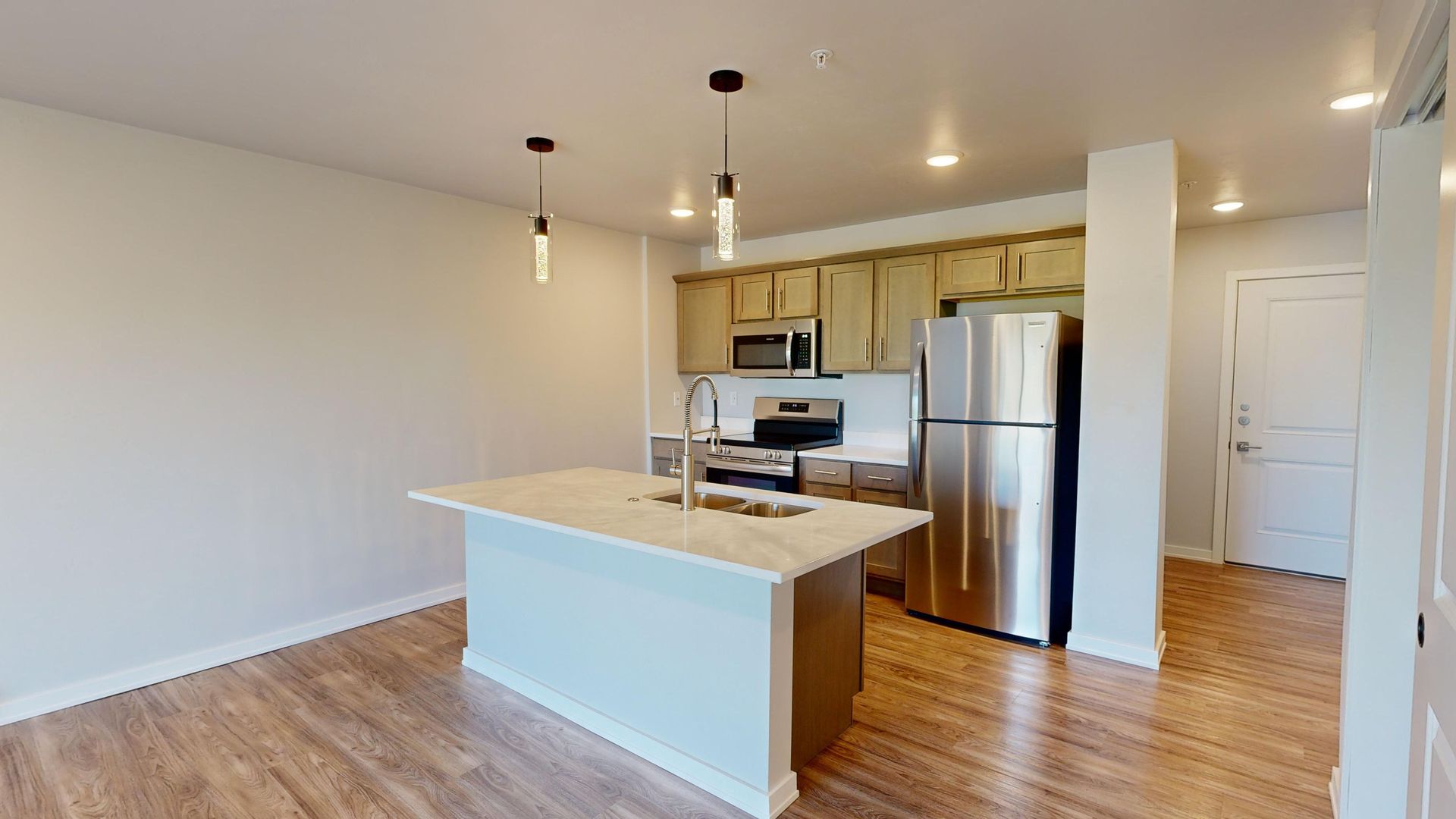 Modern kitchen with white island, stainless steel appliances, and wood floors in an open room