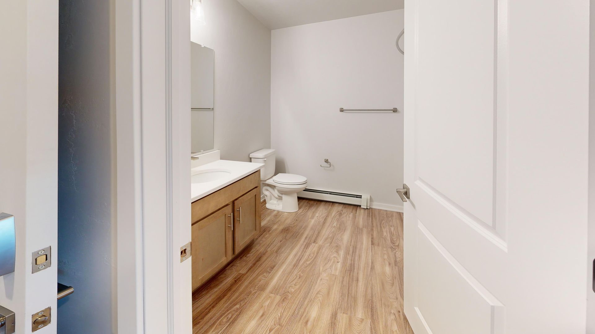 Empty exam room with an exam table, wood floor, and open white door