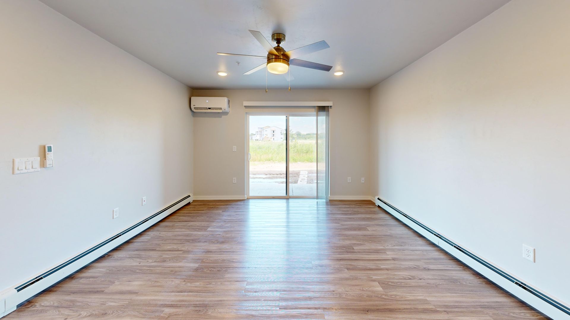Empty living room with wood floors, ceiling fan, and sliding glass doors opening to a patio.