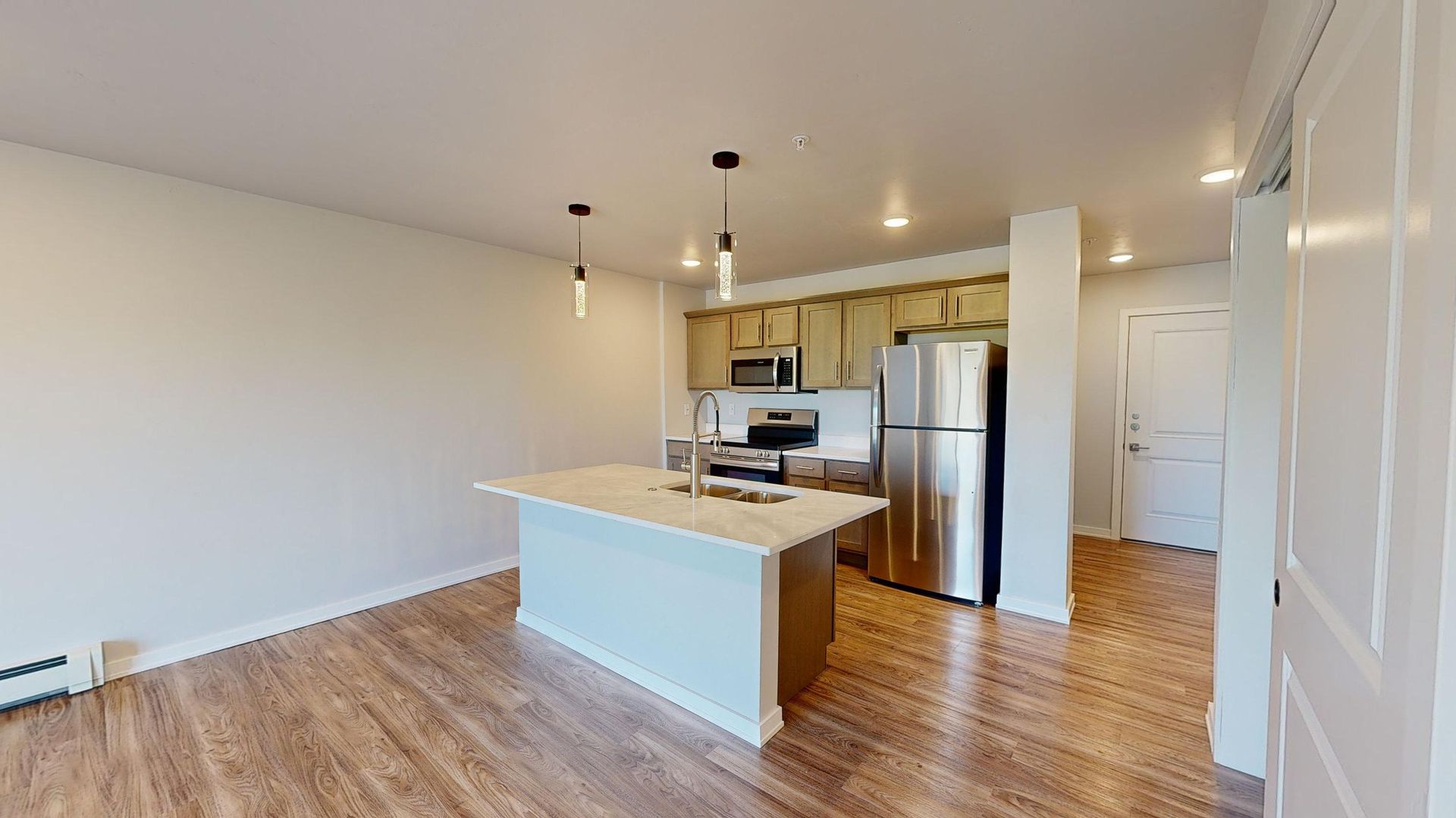 Bright modern kitchen and living area with white island, wood floors, and stainless steel appliances