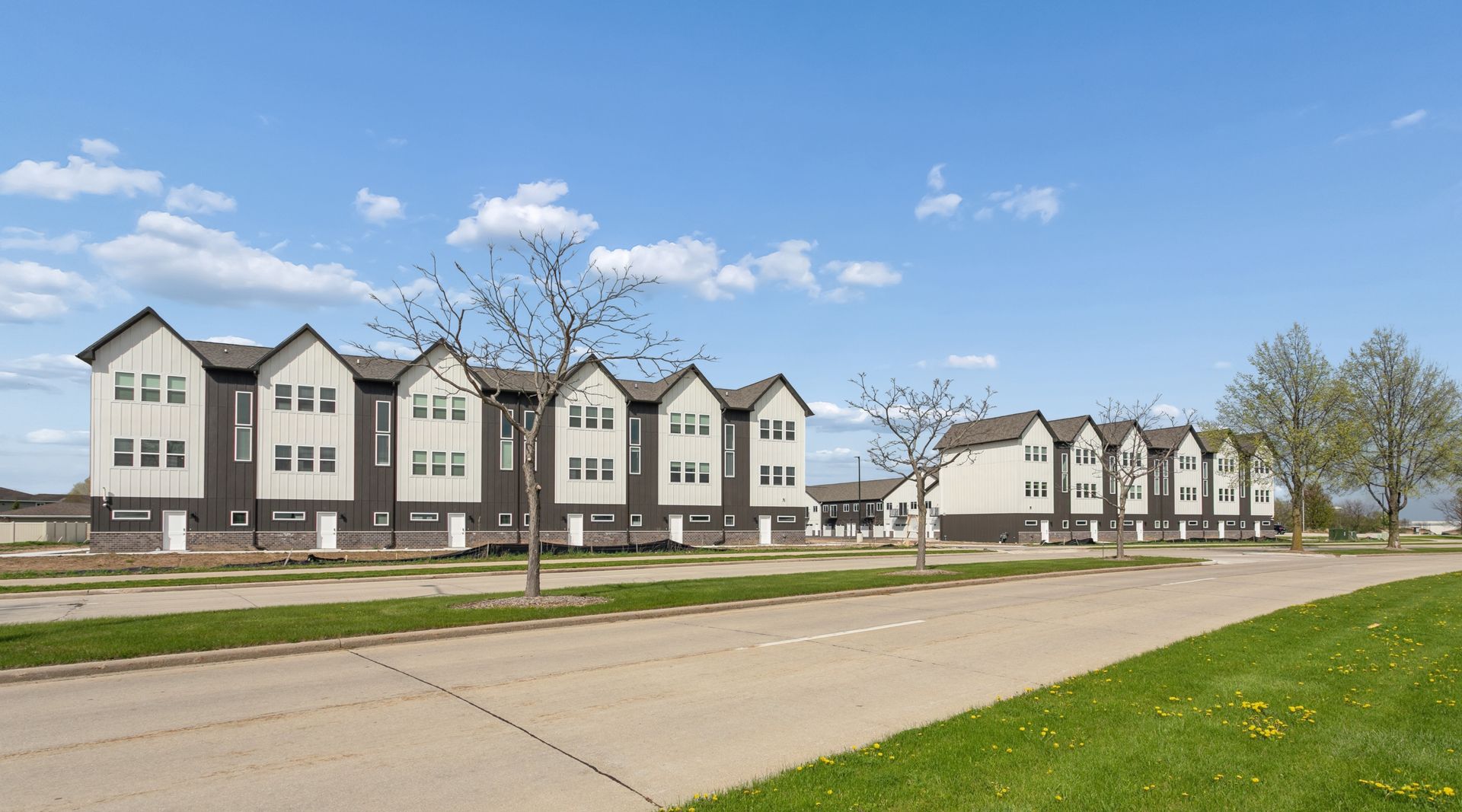 Row of modern white townhouses beside a wide road under a blue sky