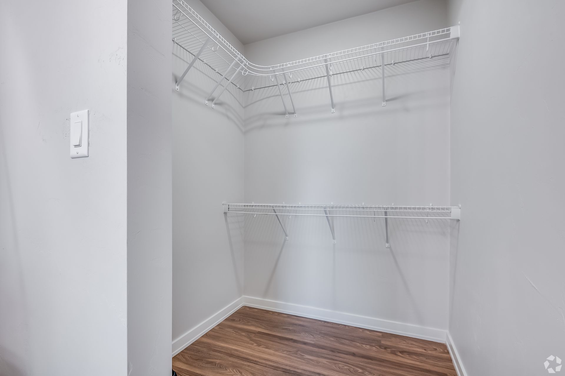 Empty white walk-in closet with wire shelves and wood flooring