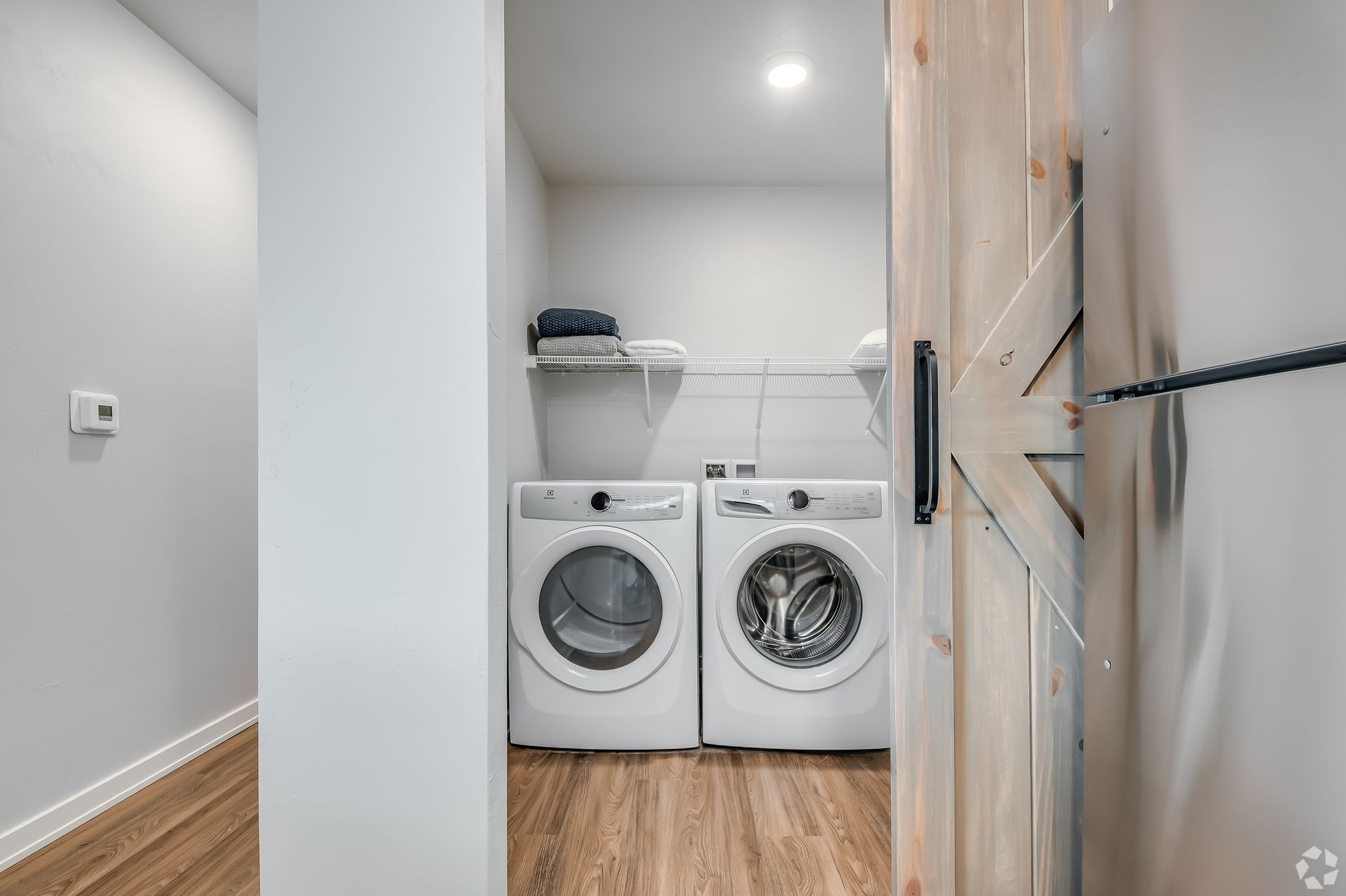 Small laundry closet with a washer, dryer, wall shelf, and wood cabinets.