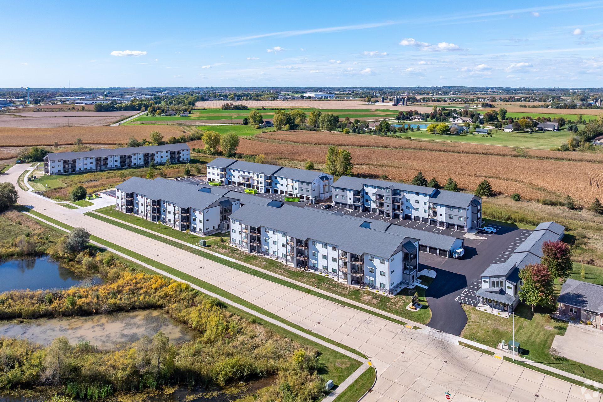 Aerial view of a modern apartment complex beside open fields on a sunny day