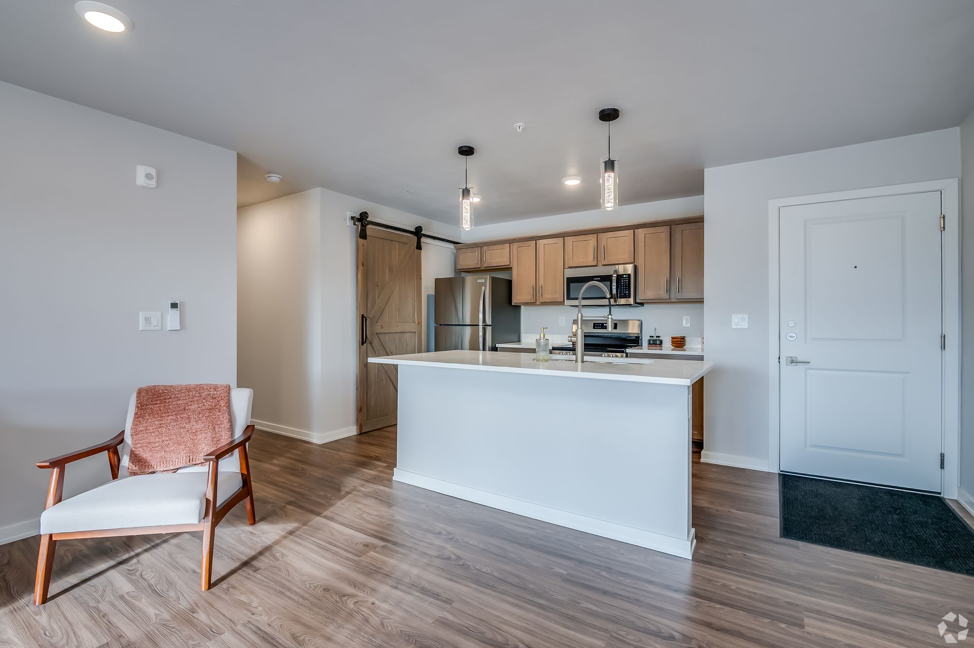 Bright apartment kitchen with white island, wood cabinets, and a chair near the entryway.