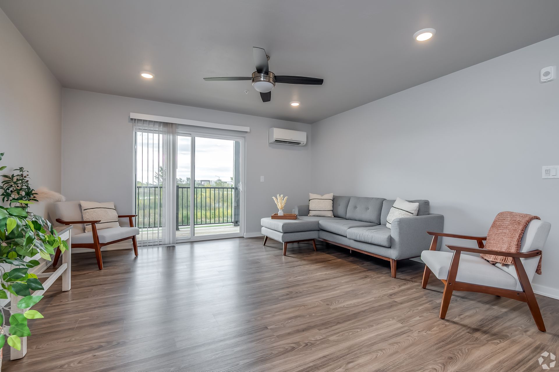 Modern living room with gray sofa, wood floor, and sliding glass doors to a balcony.