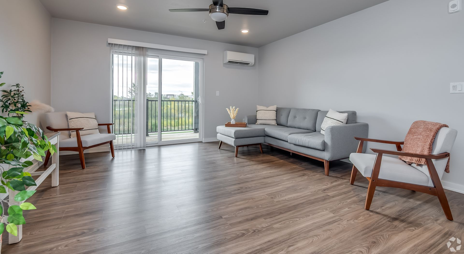 Bright living room with gray sofa, wood floor, chairs, and sliding doors to a balcony