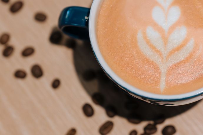 Latte with heart latte art in a dark mug on a wooden table scattered with coffee beans