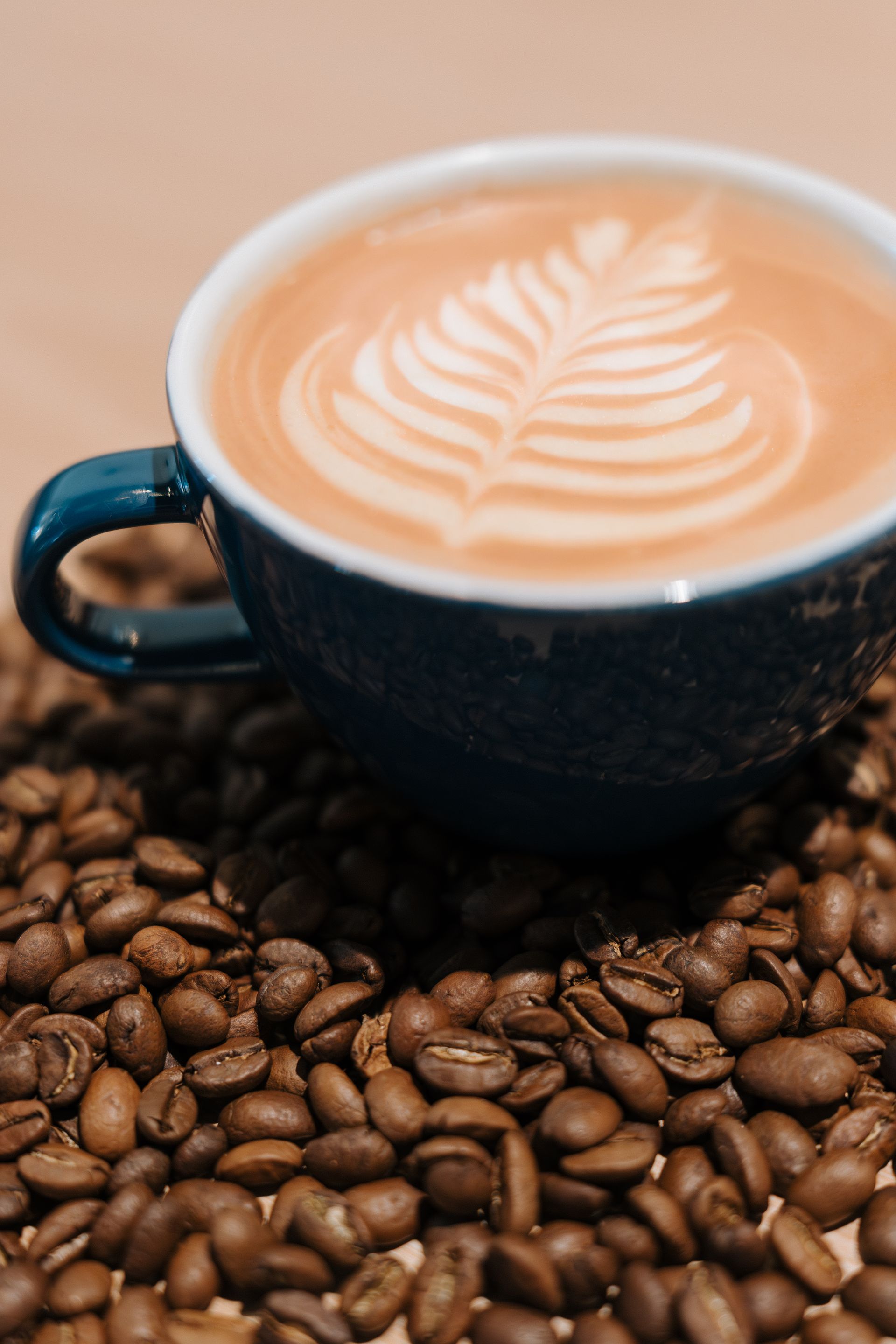 Latte with leaf art in a blue cup on a bed of coffee beans