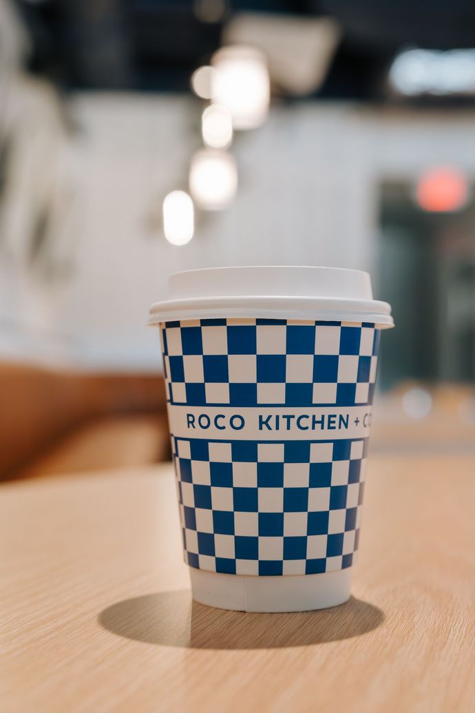Blue-and-white checkered POCO Kitchen coffee cup on a table with blurred café lights in the background