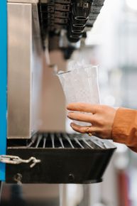 Hand filling a clear plastic cup at a soda fountain dispenser