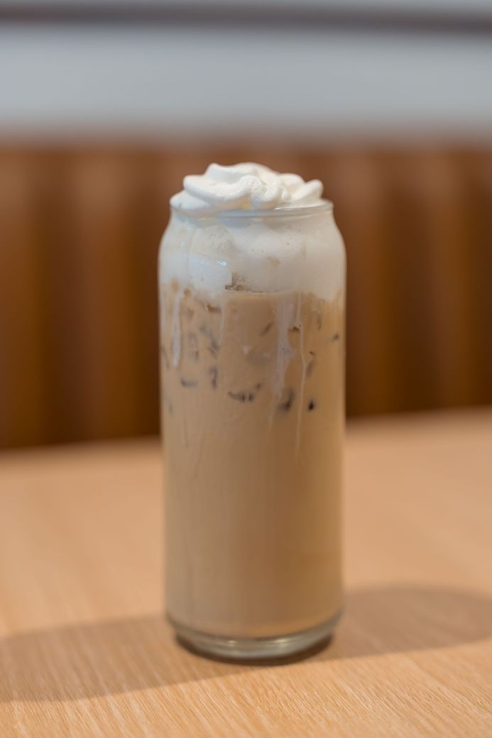 Iced coffee in a tall glass topped with whipped cream on a wooden table