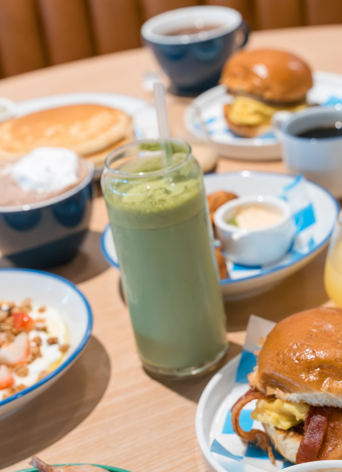 Breakfast spread with green smoothie, coffee cups, pastries, and toast on a table