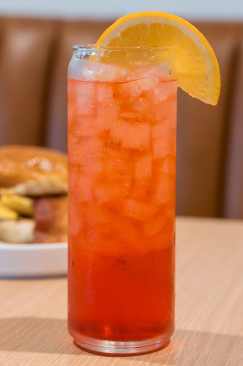 Tall orange iced drink with an orange slice garnish on a wooden table