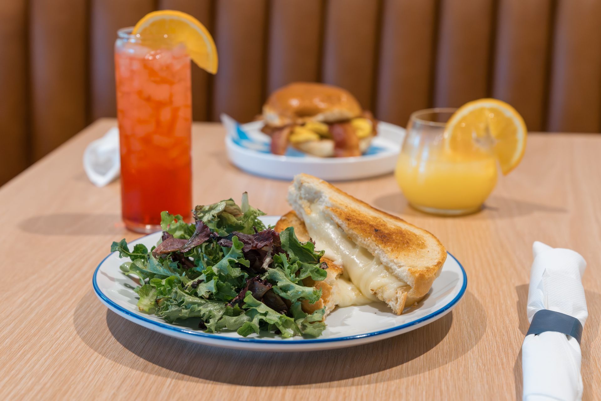 Breakfast plate with greens and toast, two orange drinks, and a sandwich on a wooden table