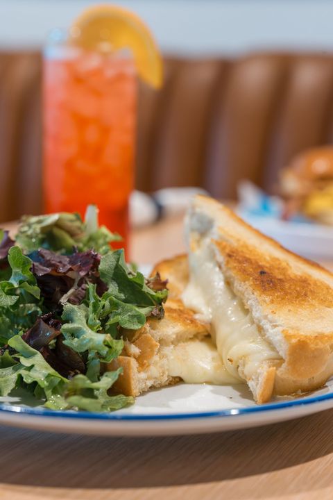 Grilled sandwich with side salad on a plate beside a tall orange drink