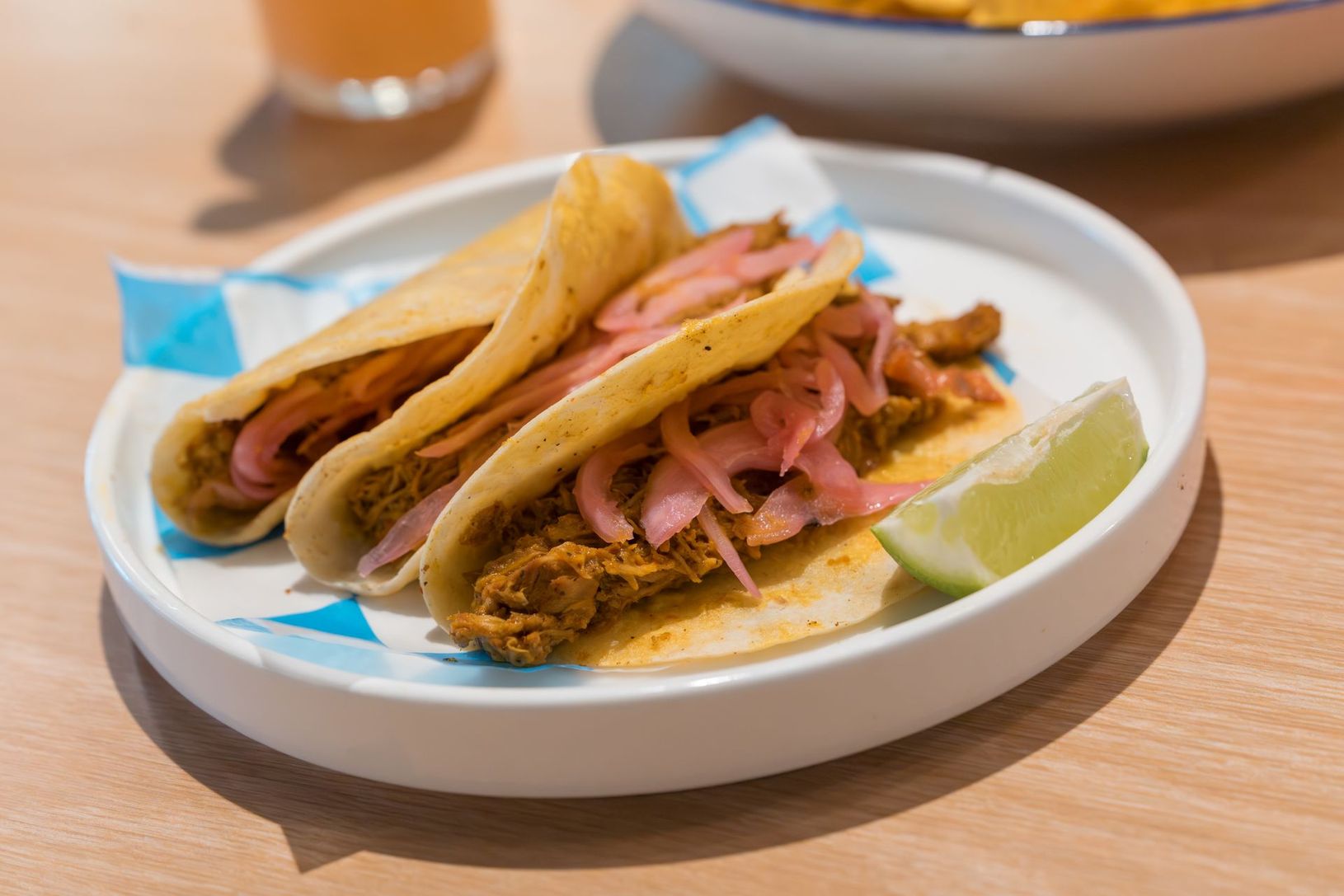 Plate of two tacos with pink pickled onions and a lime wedge on a wooden table