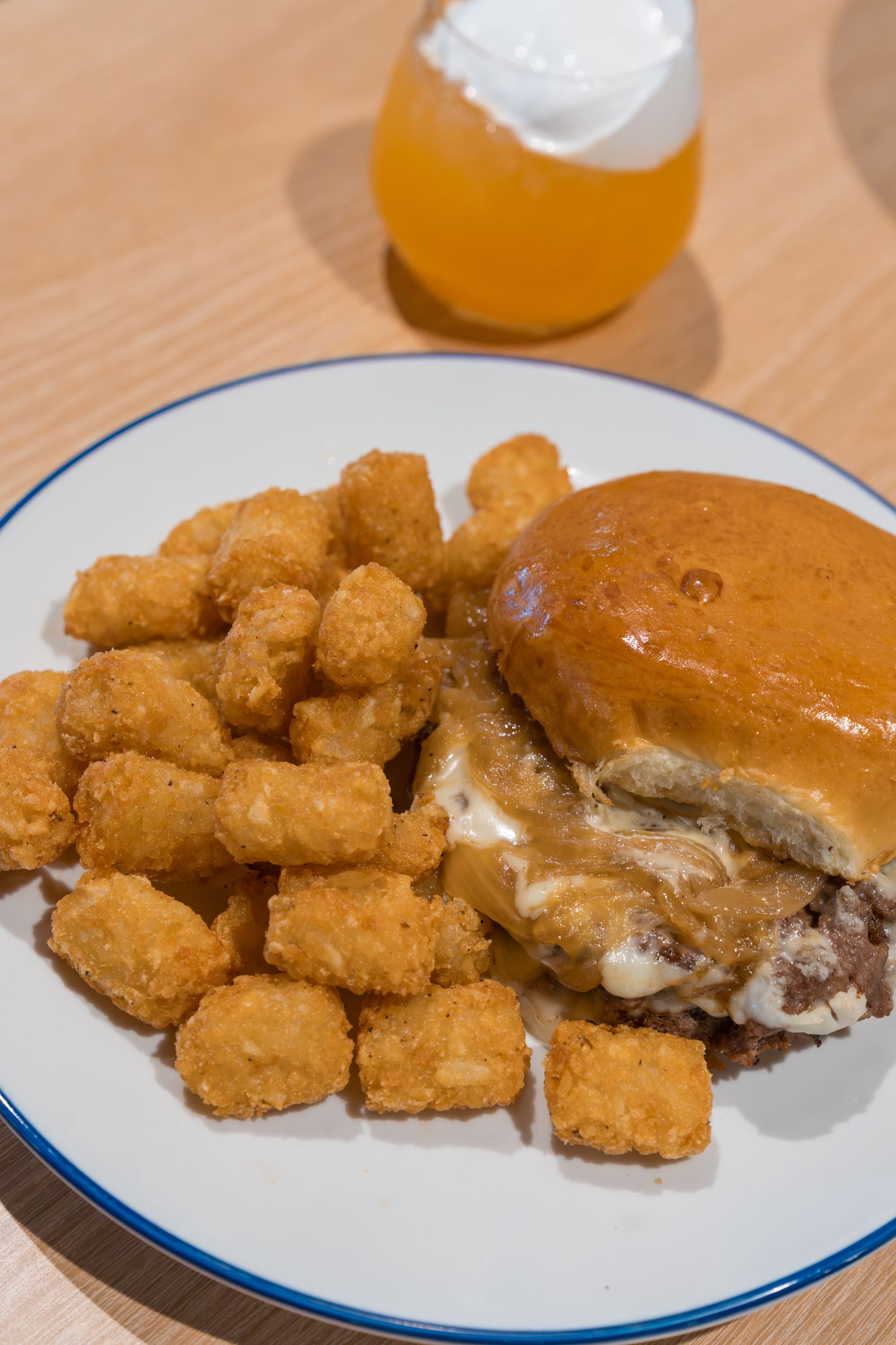 Plate with fried cubes, a sandwich bun, and a drink on a wooden table