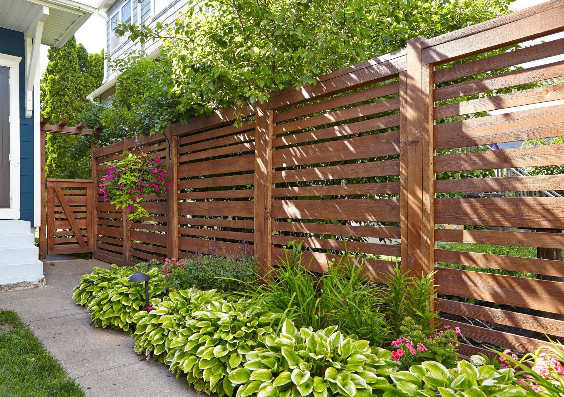 A wooden fence surrounds a lush green garden in front of a house.