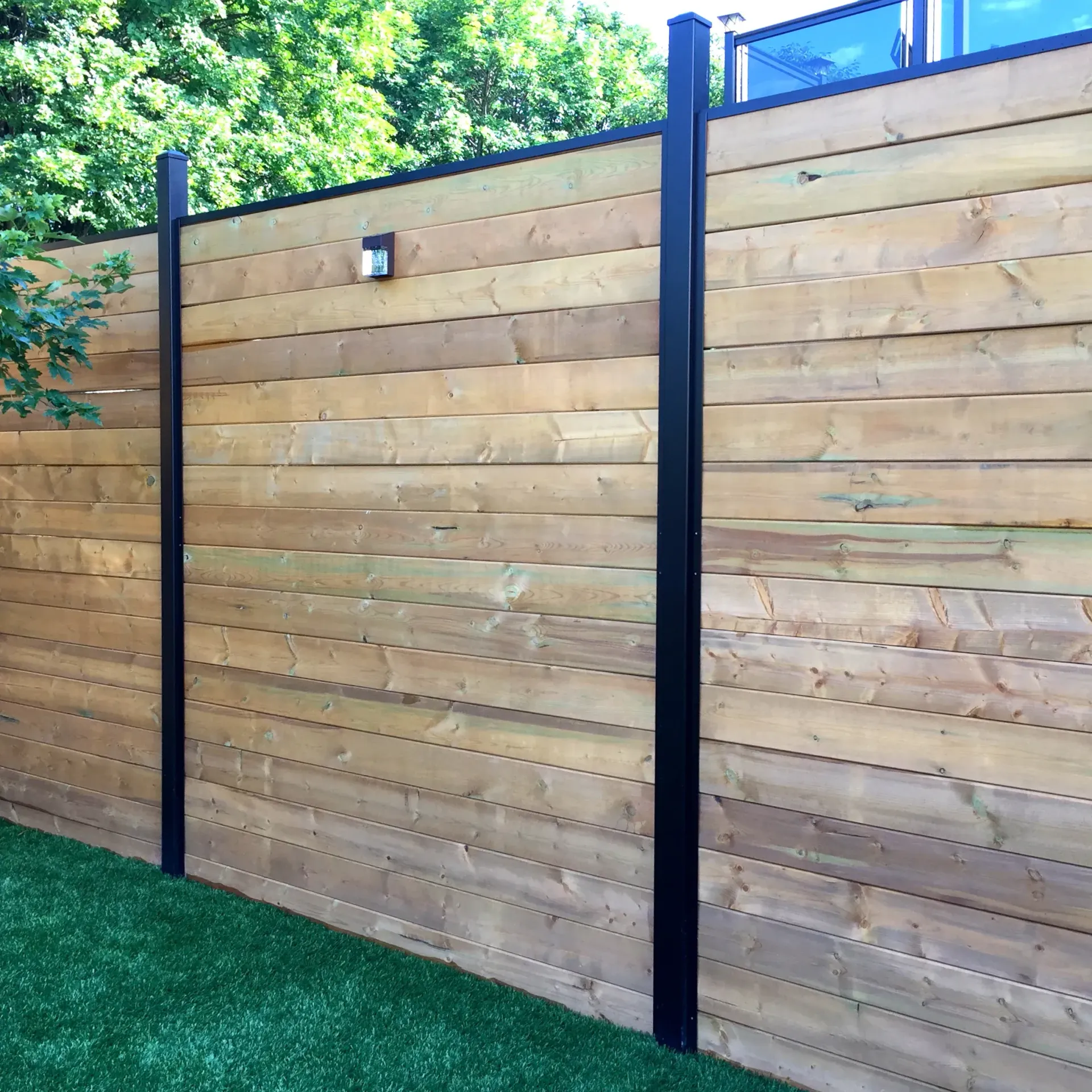 A wooden fence with black posts is surrounded by grass and trees.