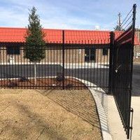A black fence is in front of a building with a red roof.