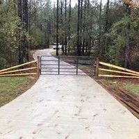 A concrete driveway with a metal gate and a wooden fence.