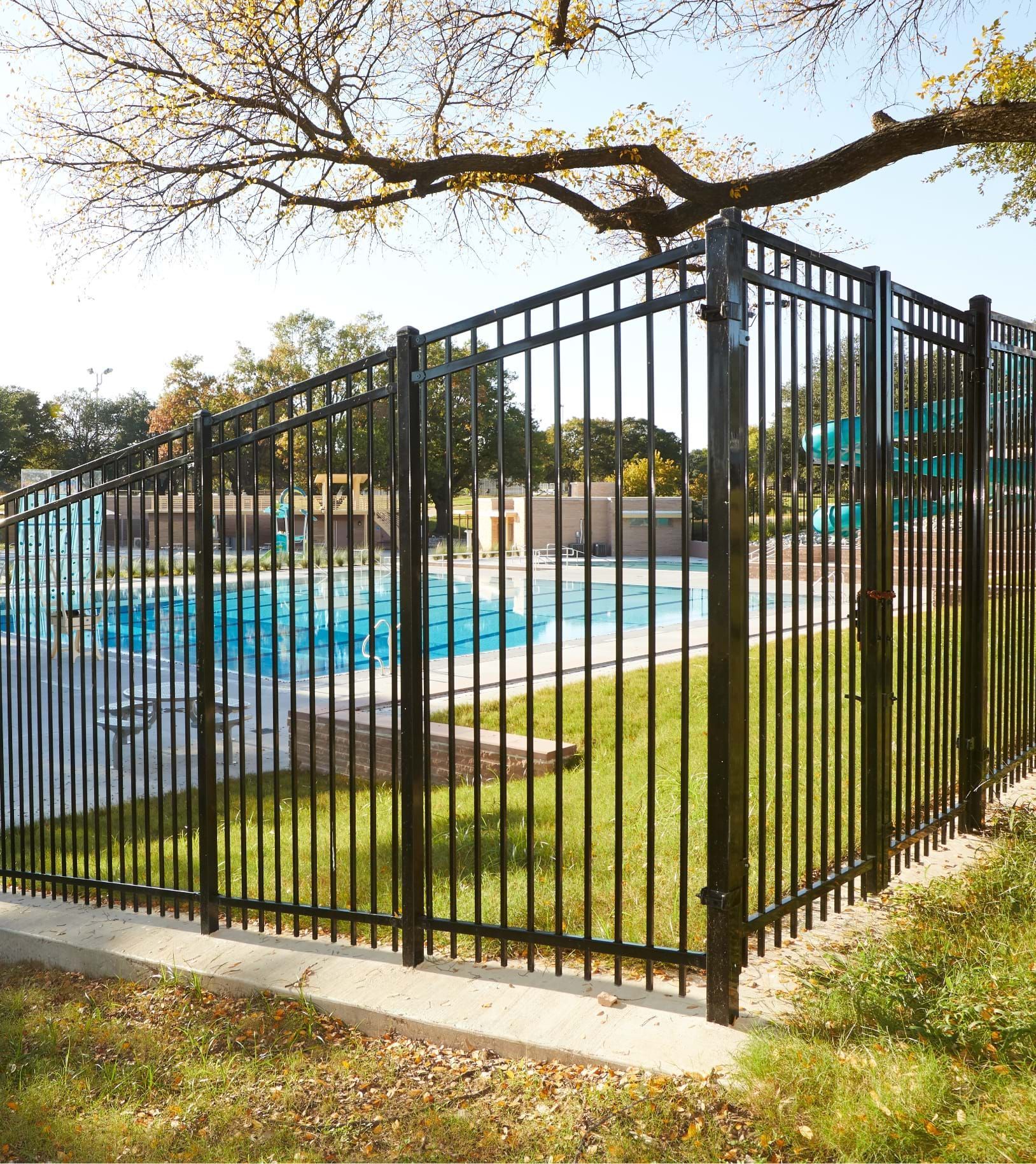 A black metal fence surrounds a swimming pool in a park