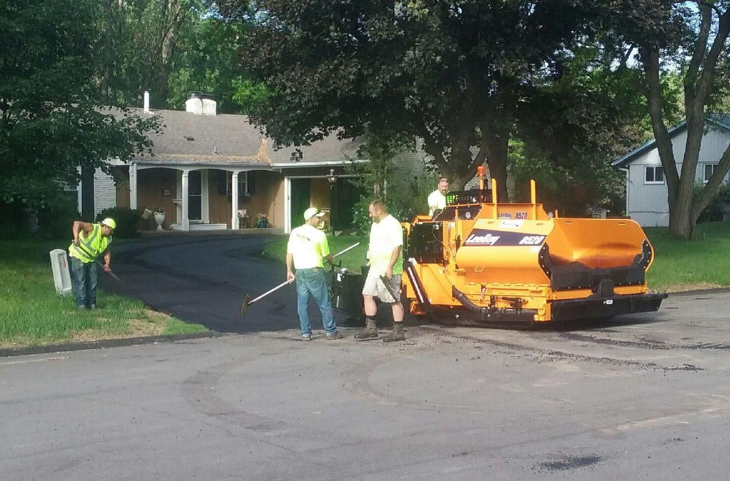 A group of men are working on a driveway in front of a house