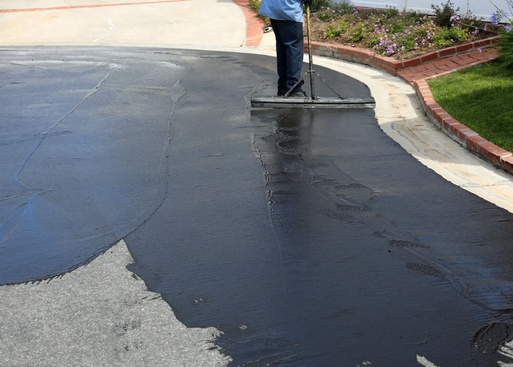 A man is spreading asphalt on a driveway with a broom.