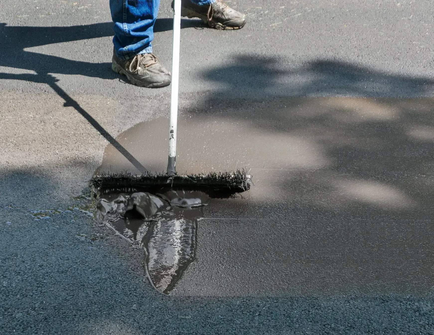 A person is spreading asphalt on the ground with a broom.