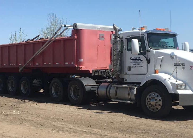A white semi truck with a red dump trailer is parked in a dirt lot.