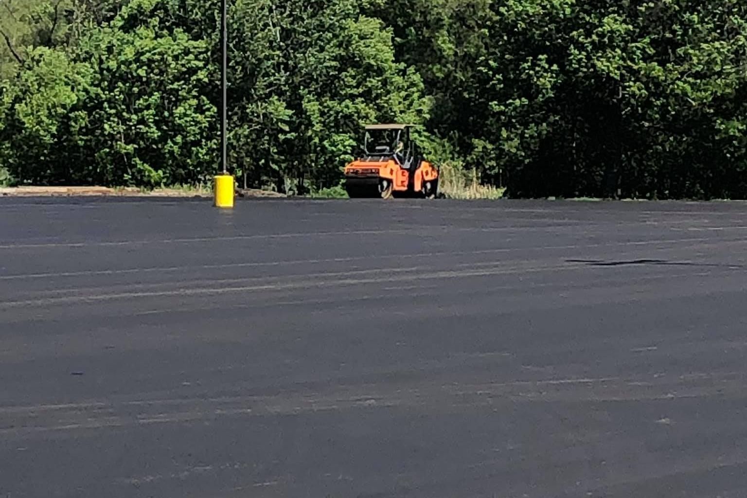 A roller is rolling asphalt in a parking lot.