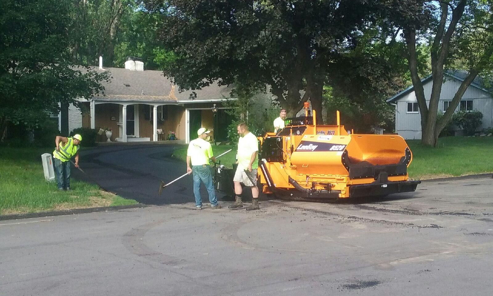 A group of people are working on a driveway in front of a house