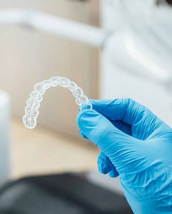 Hand in blue glove holding a clear dental aligner in a dental office.