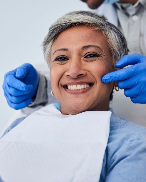 Dentist examining a patient's teeth with tools, the patient wearing protective glasses, indoor setting.