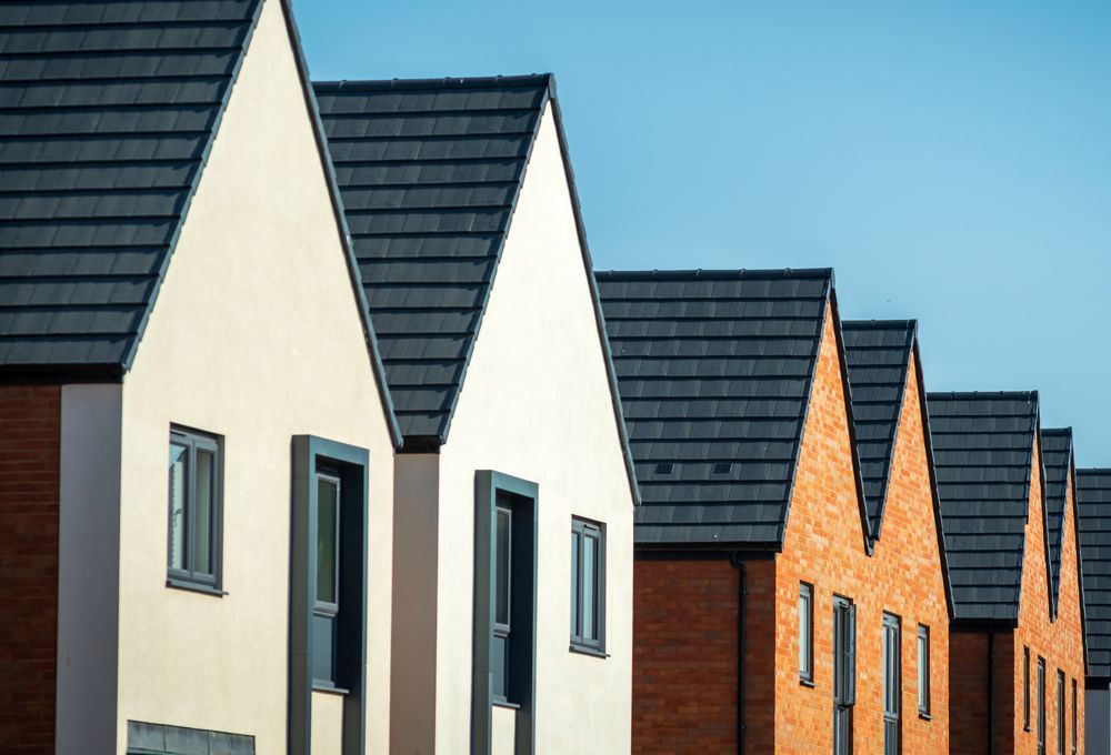 Row of modern houses with dark roofs and white and brick facades under a clear blue sky
